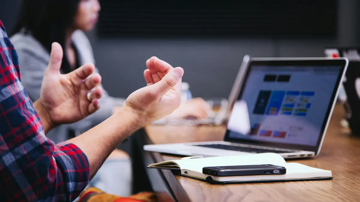 Colleagues talking across a table with an open laptop between them